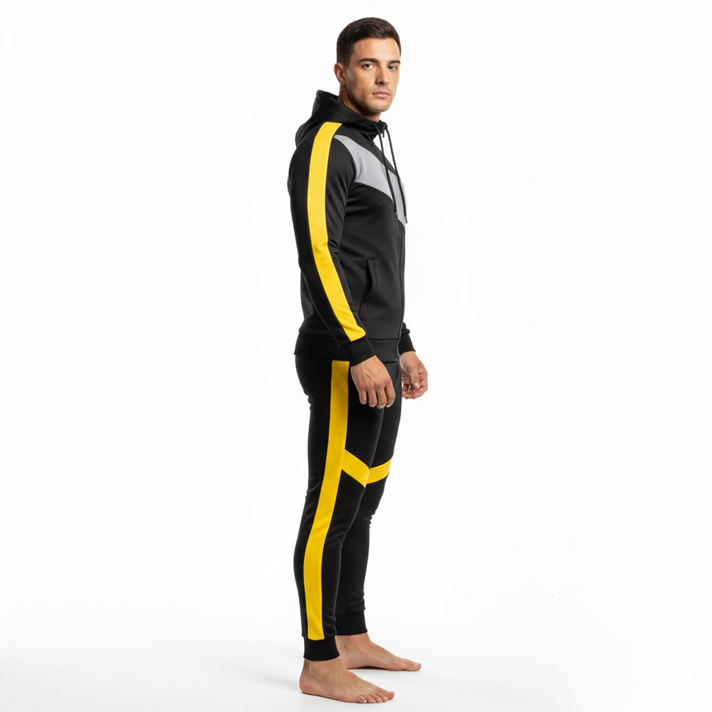 Man wearing a black and yellow two-piece athletic outfit with a hooded sweatshirt and matching track pants, standing barefoot in a studio pose.